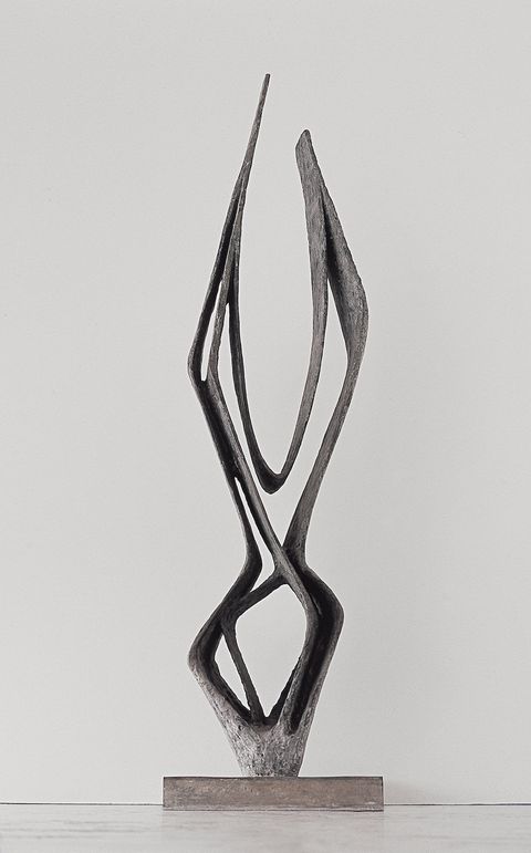 Sculpture. Strips of bronze are fashioned into an abstract shape. Several bands expand from a point at the bottom and create a diamond shape. The taller part above is like a flickering candle flame.