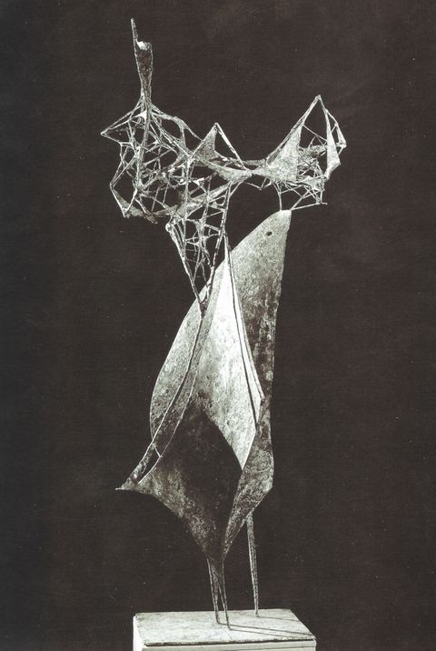 Sculpture. Black and white photograph of a bronze, abstract form. An elongated, triangular piece resting on three pointed legs is reminiscent of an animal or bird, a beak or muzzle stretched up. A cloud like a spider’s web whipped in wind rises above.